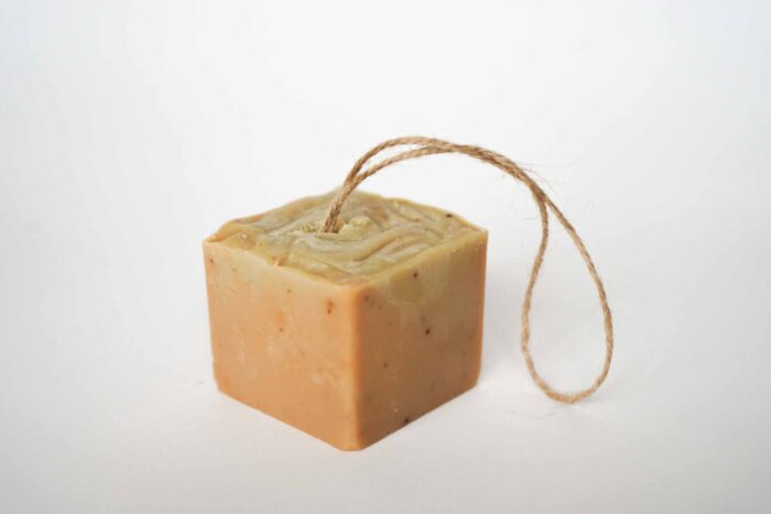 NYEMLO | Relief Unscented Soap | Papaya & Oats - Cube A square, beige bar of soap with a rough texture and a looped jute string embedded at the top, set against a plain white background.