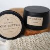 2 cans. one with body butter and one with body scrub pictured on a piece of wood