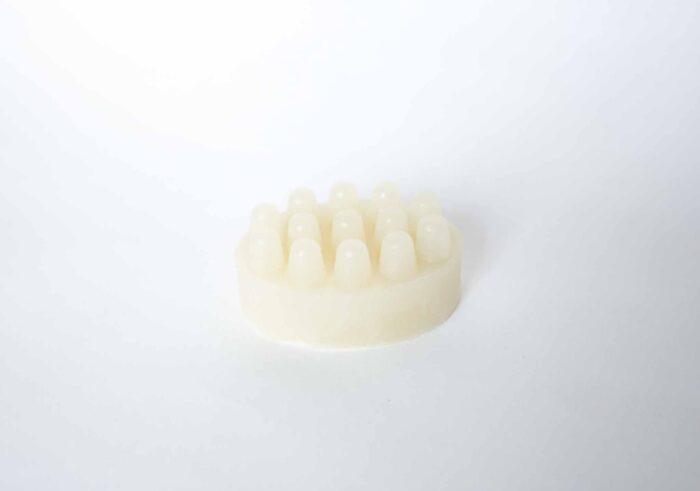 A moisturizing shampoo bar with a unique shape, resembling a piece of a honeycomb, in a soft cream color suggesting its mango scent and rich blend of nourishing oils.