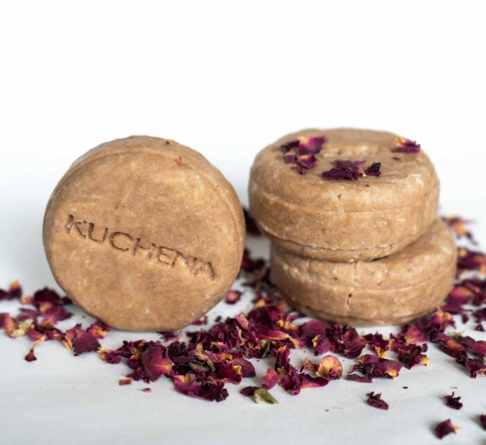 Three round detox shampoo bars with the word "KUCHENA" embossed, stacked in the background with rose petals scattered around on a white background.