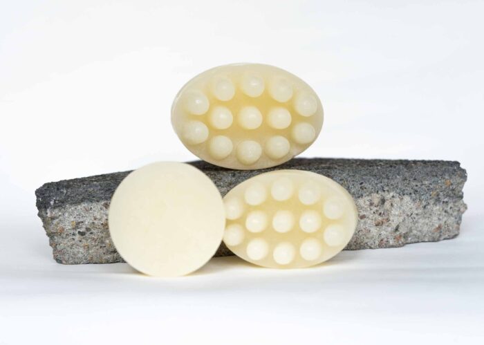 Three pale yellow massage shampoo bars with raised nodules, displayed on a natural gray stone against a white background.